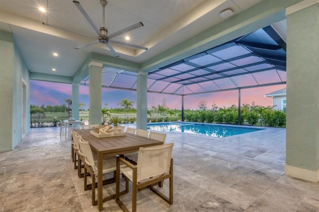 pool at dusk featuring glass enclosure, ceiling fan, and a patio