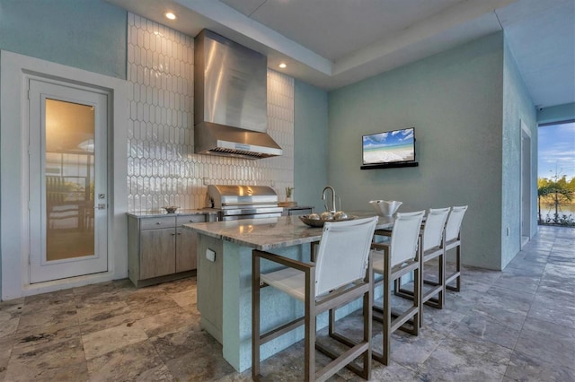 kitchen featuring backsplash, light stone counters, wall chimney exhaust hood, and sink