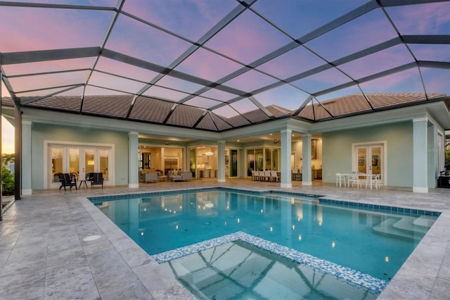 pool at dusk featuring a patio area, a lanai, an outdoor hangout area, and french doors