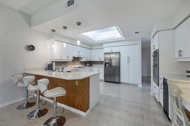 kitchen with kitchen peninsula, stainless steel appliances, sink, white cabinetry, and hanging light fixtures