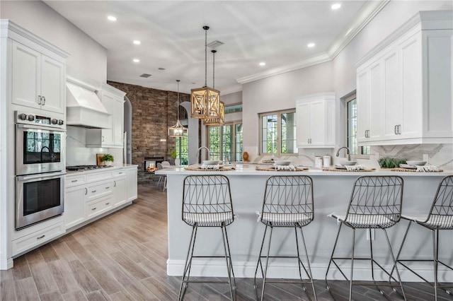 kitchen with kitchen peninsula, custom exhaust hood, stainless steel appliances, decorative light fixtures, and a breakfast bar area