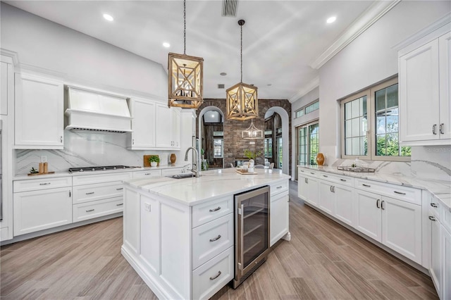 kitchen featuring light stone counters, custom exhaust hood, pendant lighting, white cabinets, and wine cooler