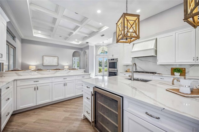 kitchen featuring wine cooler, white cabinetry, decorative light fixtures, and custom range hood