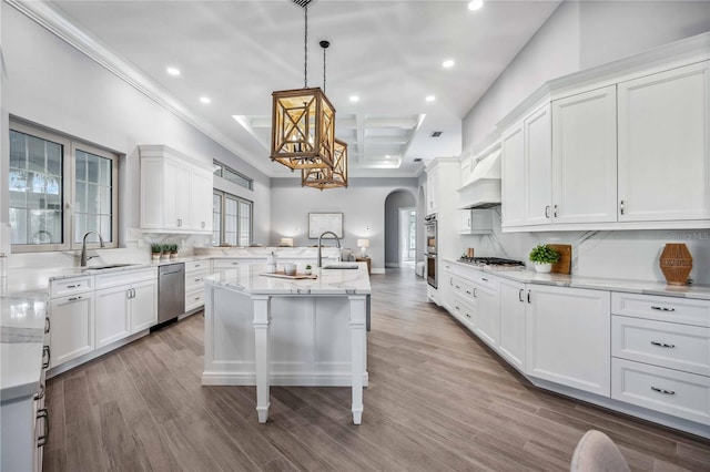 kitchen with custom exhaust hood, backsplash, a kitchen island with sink, decorative light fixtures, and a kitchen bar