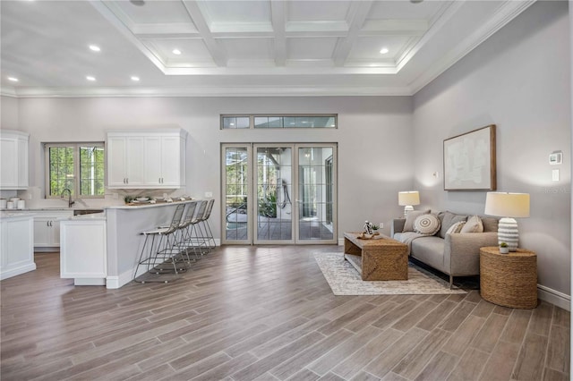 living room with beam ceiling, light hardwood / wood-style flooring, coffered ceiling, and ornamental molding