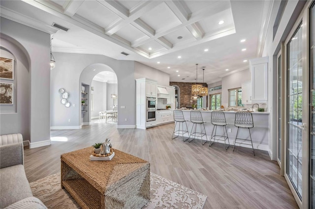 living room featuring light wood-type flooring, ornamental molding, coffered ceiling, beam ceiling, and a chandelier