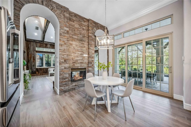 dining room with light hardwood / wood-style floors, a stone fireplace, ornamental molding, and a chandelier