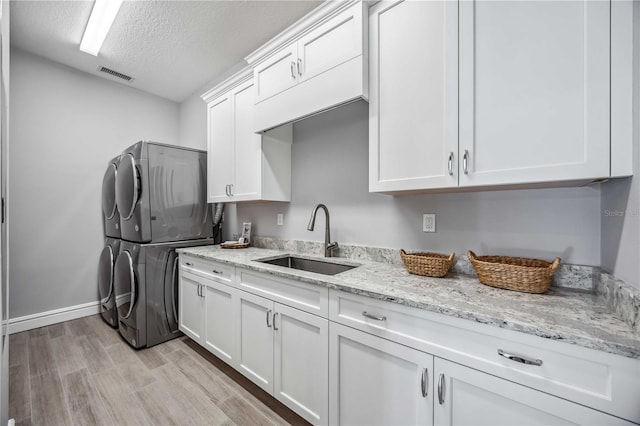 kitchen with light stone countertops, stacked washing maching and dryer, a textured ceiling, sink, and white cabinets