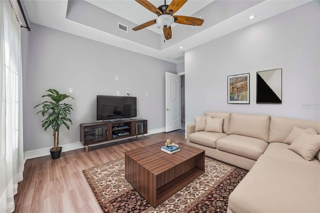 living room with light wood-type flooring, a raised ceiling, and ceiling fan