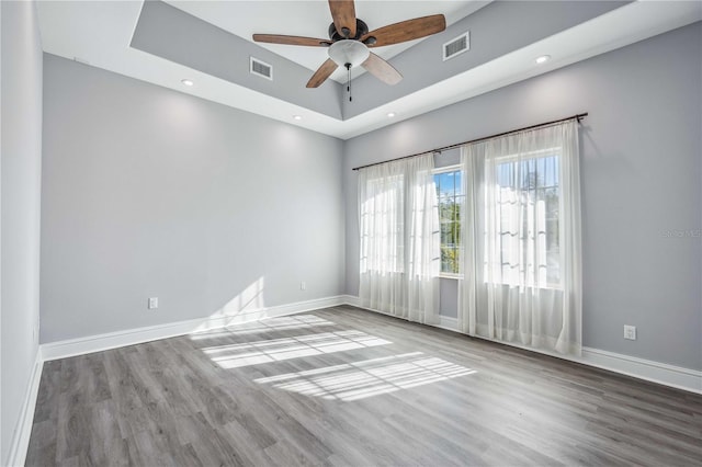 empty room with hardwood / wood-style floors, ceiling fan, and a raised ceiling