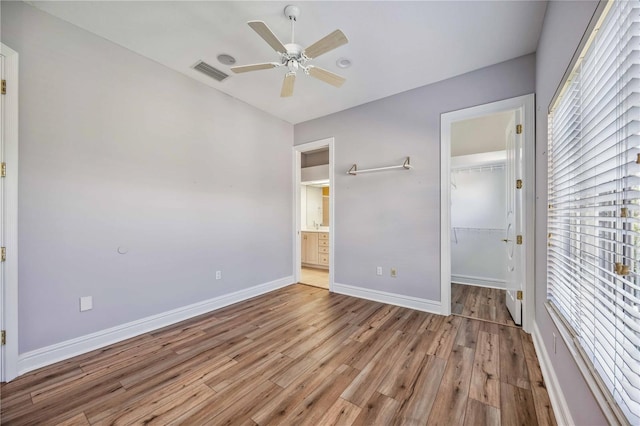 unfurnished bedroom with light wood-type flooring, a walk in closet, a closet, and ceiling fan