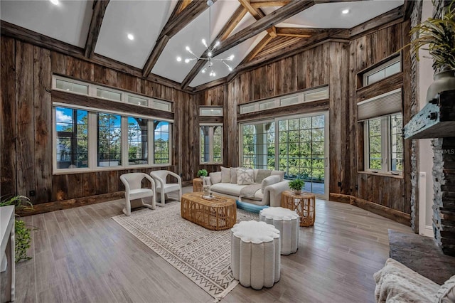 living room featuring beamed ceiling, a notable chandelier, wooden walls, and high vaulted ceiling