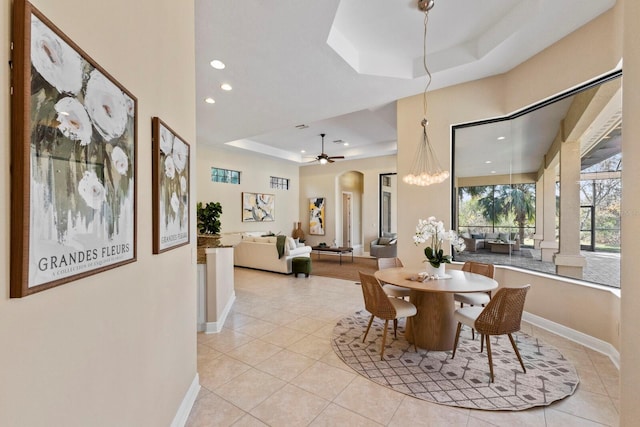 dining area with light tile patterned flooring, a tray ceiling, and ceiling fan with notable chandelier