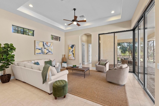 tiled living room with a tray ceiling and ceiling fan