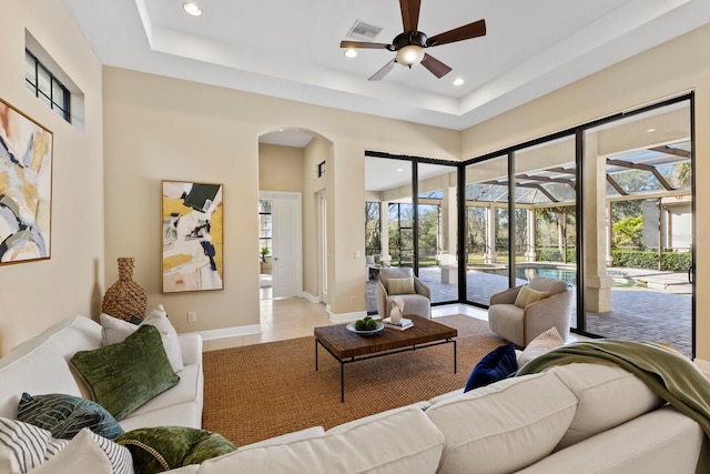 living room featuring light tile patterned floors, a raised ceiling, ceiling fan, and a high ceiling