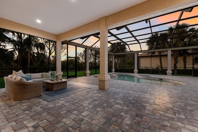 pool at dusk featuring outdoor lounge area, a patio, and glass enclosure