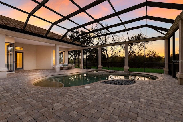 pool at dusk featuring a patio area, glass enclosure, and an in ground hot tub