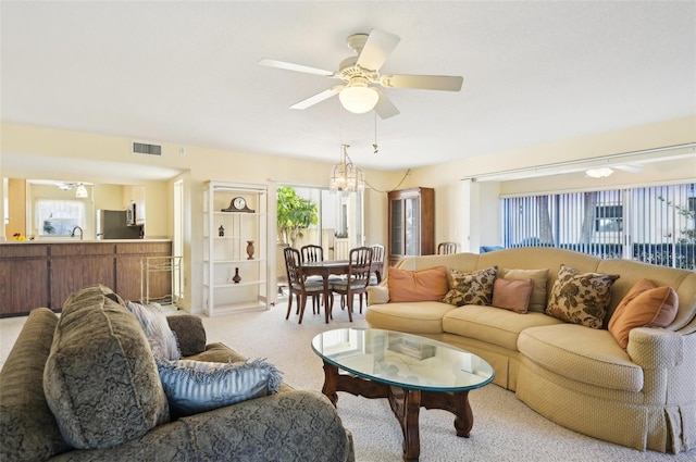 carpeted living room with a wealth of natural light and ceiling fan with notable chandelier