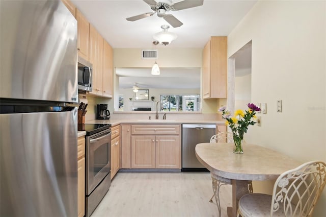 kitchen with sink, light wood-type flooring, light brown cabinetry, appliances with stainless steel finishes, and kitchen peninsula