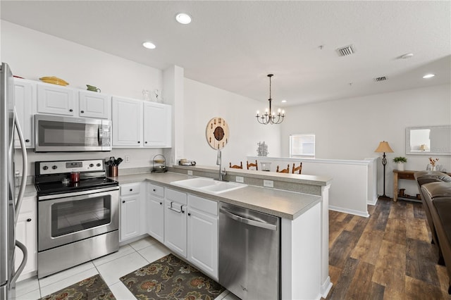 kitchen with white cabinetry, sink, stainless steel appliances, an inviting chandelier, and kitchen peninsula