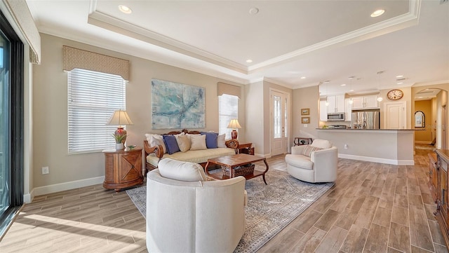 living room with light wood-type flooring, a raised ceiling, and ornamental molding