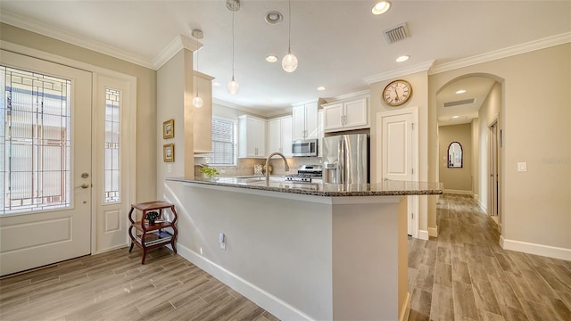 kitchen with hanging light fixtures, light hardwood / wood-style flooring, kitchen peninsula, white cabinets, and appliances with stainless steel finishes