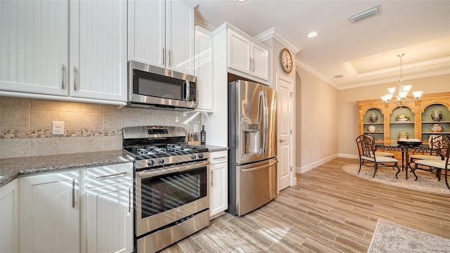 kitchen with white cabinets, crown molding, stainless steel appliances, and a chandelier