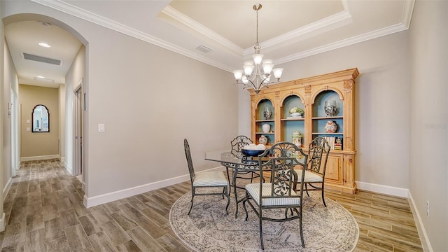 dining space with a raised ceiling, crown molding, and a notable chandelier