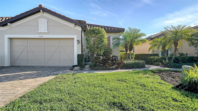 view of front facade with a tile roof, decorative driveway, an attached garage, a front yard, and stucco siding