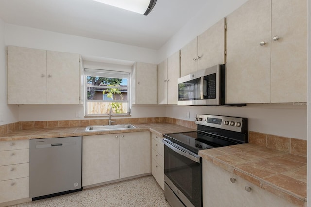 kitchen with tile counters, stainless steel appliances, a sink, and light speckled floor