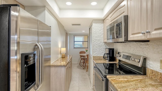 kitchen featuring a raised ceiling, light tile patterned floors, light brown cabinetry, appliances with stainless steel finishes, and light stone counters