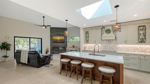 kitchen with an island with sink, a skylight, sink, and custom exhaust hood