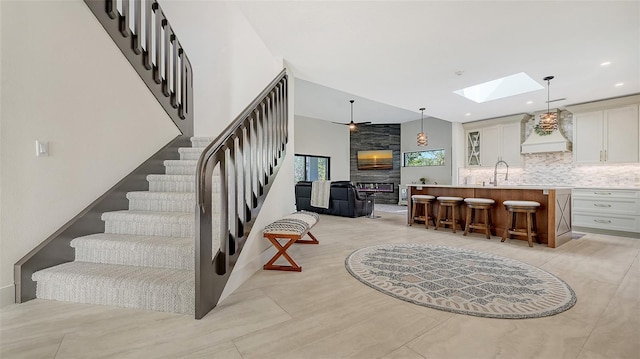 stairs featuring sink, a large fireplace, ceiling fan, and a skylight