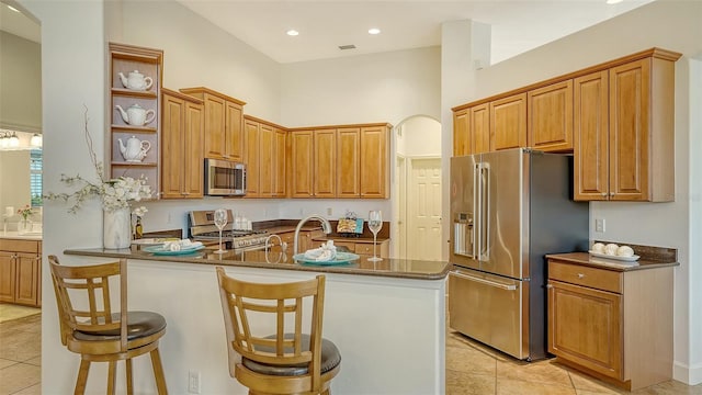 kitchen with a kitchen breakfast bar, a towering ceiling, a kitchen island with sink, light tile patterned flooring, and appliances with stainless steel finishes