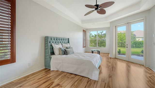 bedroom featuring french doors, access to outside, a tray ceiling, ceiling fan, and light hardwood / wood-style floors