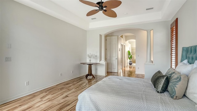 bedroom with light hardwood / wood-style flooring, a raised ceiling, and ceiling fan