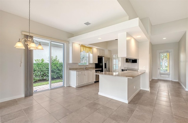 kitchen with kitchen peninsula, appliances with stainless steel finishes, light stone counters, a notable chandelier, and white cabinets