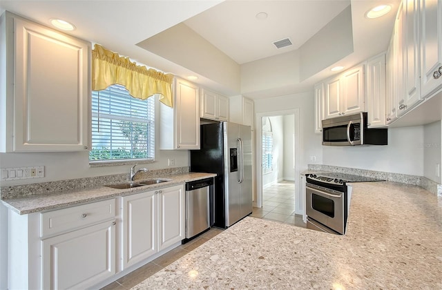 kitchen with appliances with stainless steel finishes, a raised ceiling, sink, light tile patterned floors, and white cabinets