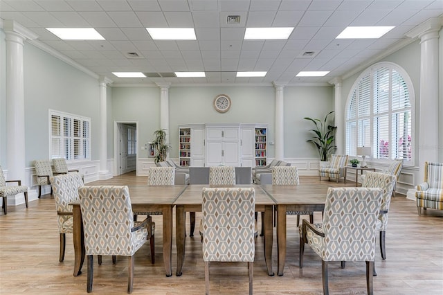 dining room with light hardwood / wood-style floors, ornamental molding, and decorative columns