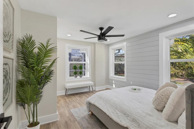 bedroom featuring multiple windows, ceiling fan, wood walls, and light wood-type flooring