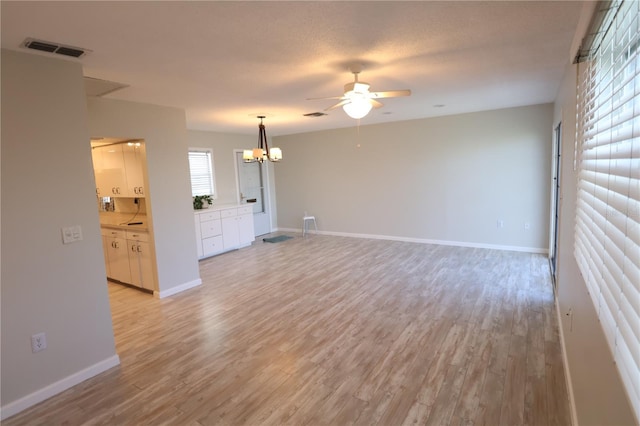 unfurnished living room with ceiling fan with notable chandelier and light hardwood / wood-style floors