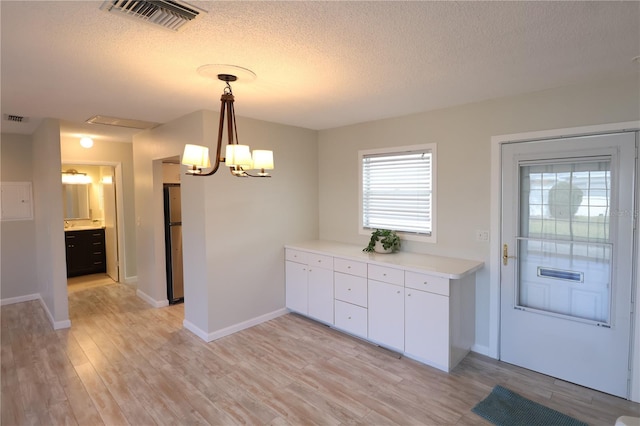 kitchen featuring a chandelier, hanging light fixtures, light wood-type flooring, stainless steel refrigerator, and white cabinets