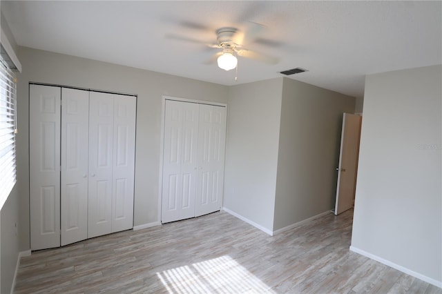 unfurnished bedroom featuring light wood-type flooring, two closets, and ceiling fan