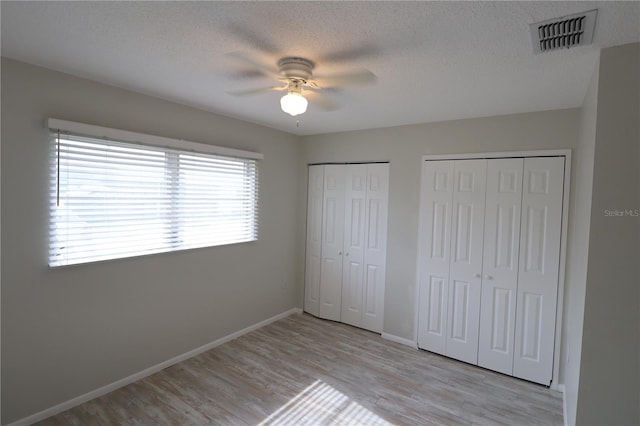 unfurnished bedroom with a textured ceiling, two closets, ceiling fan, and light hardwood / wood-style flooring