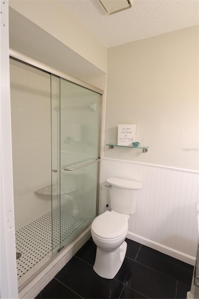 bathroom with a textured ceiling, tile patterned flooring, a shower with shower door, and toilet