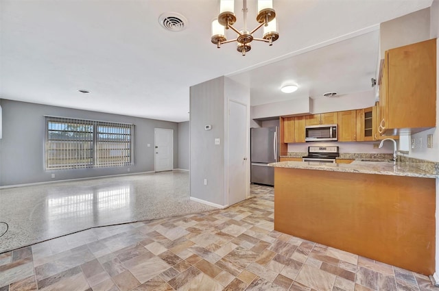 kitchen featuring light stone countertops, sink, a notable chandelier, kitchen peninsula, and appliances with stainless steel finishes