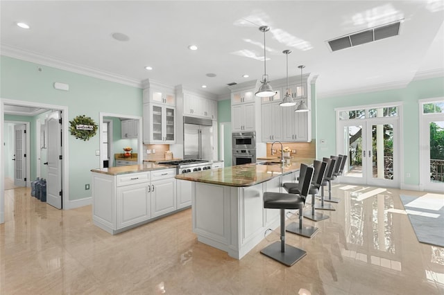 kitchen featuring a center island with sink, sink, white cabinetry, decorative light fixtures, and french doors