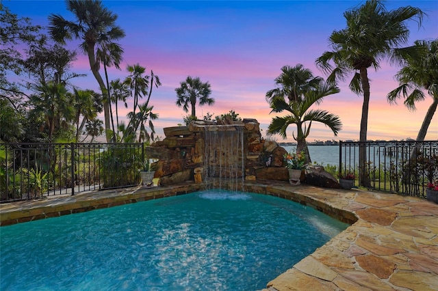 pool at dusk featuring pool water feature, a water view, and a patio area