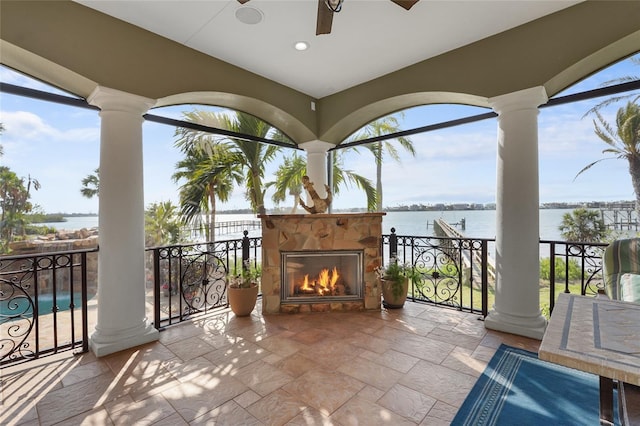 view of patio / terrace featuring an outdoor stone fireplace, a water view, and ceiling fan