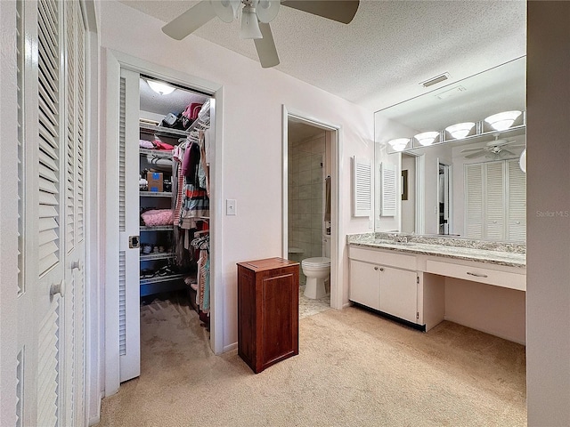 bathroom featuring vanity, a shower, ceiling fan, toilet, and a textured ceiling